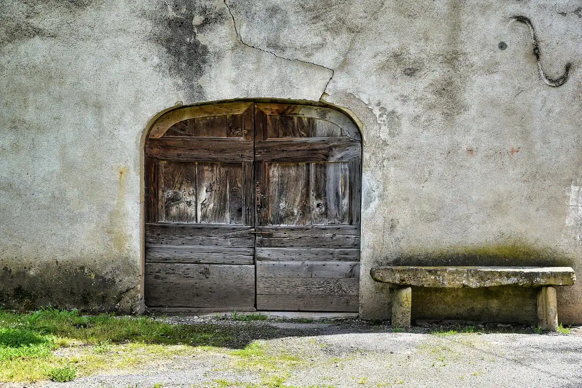 O ușă veche și o bancă lângă un perete rustic din piatră, într-o clădire îmbătrânită de vreme