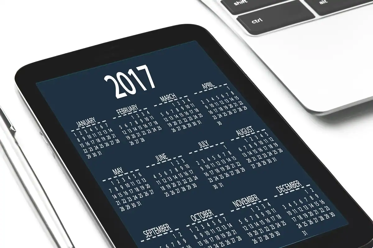 O agendă cu calendar pe un birou, lângă un telefon mobil și o tabletă, pentru planificarea lunii