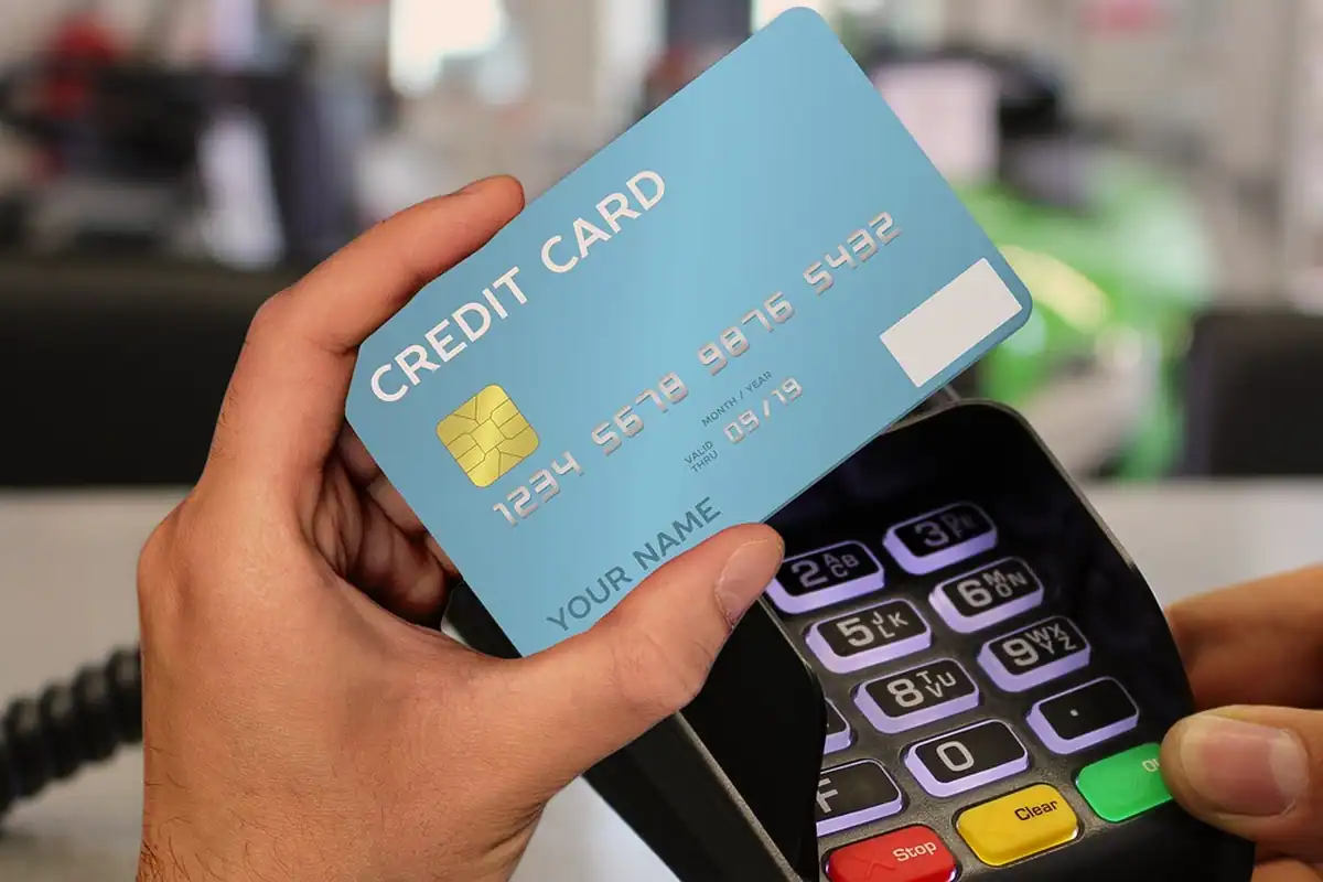 Card de credit ținut în mână lângă un terminal de plată cu tastatură