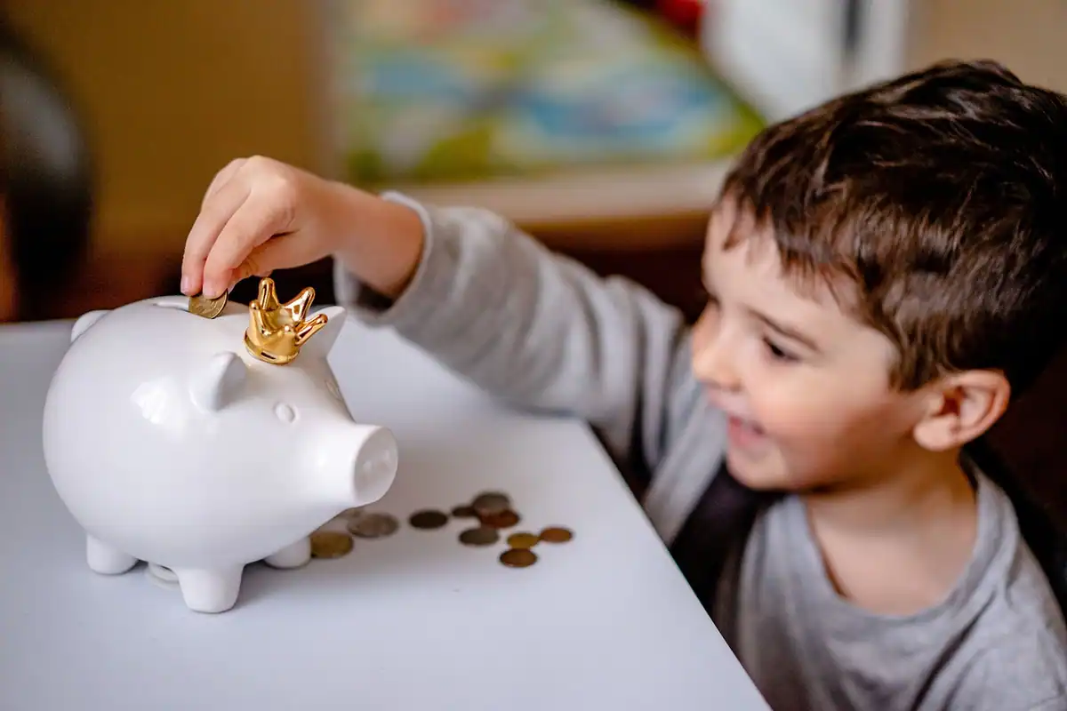 Pușculiță în formă de porc, simbol al economiilor, lângă câteva monede, pe o masă