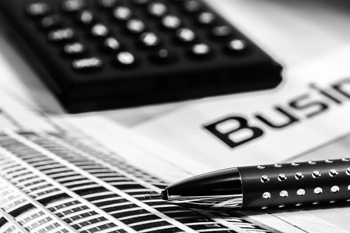 Calculator negru și pix așezate pe un ziar financiar, pentru calculul comisioanelor de credit