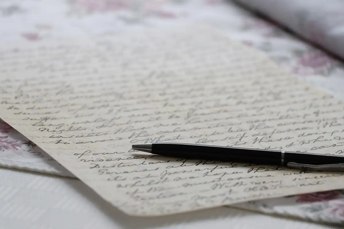 Scrisoare scrisă de mână pe hârtie veche, cu un pix alături, pentru cererea de corectare