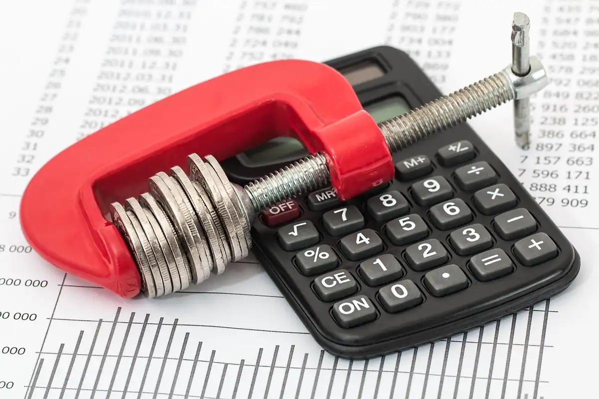 Calculator prins într-o clemă roșie cu monede, simbol al costurilor care apasă bugetul la început