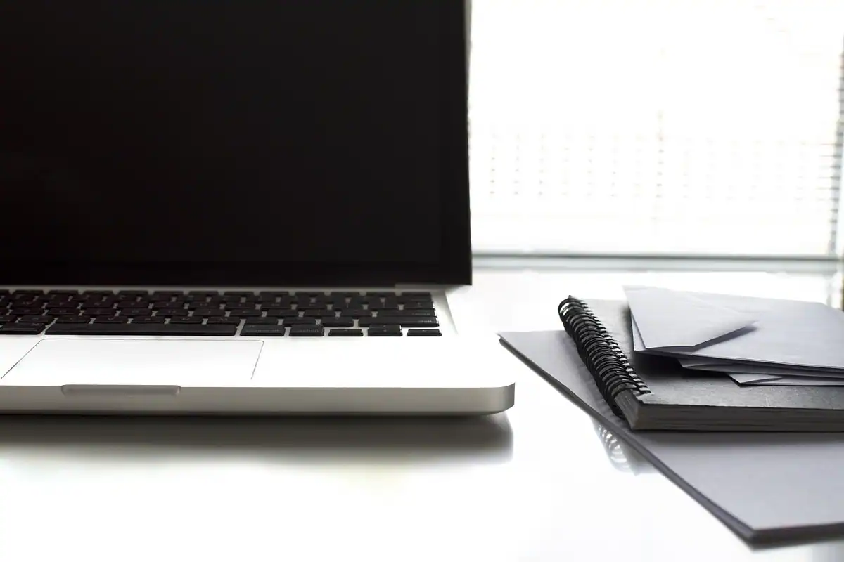 Laptop deschis și un carnet pe un birou luminos, unde se compară costurile refinanțării