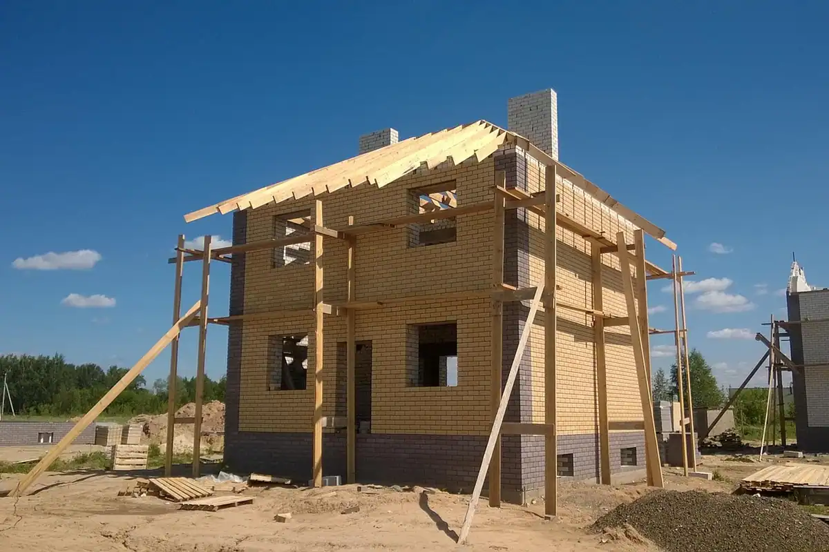 Casă din lemn cu structura acoperișului aproape gata, ridicată pe un teren nisipos