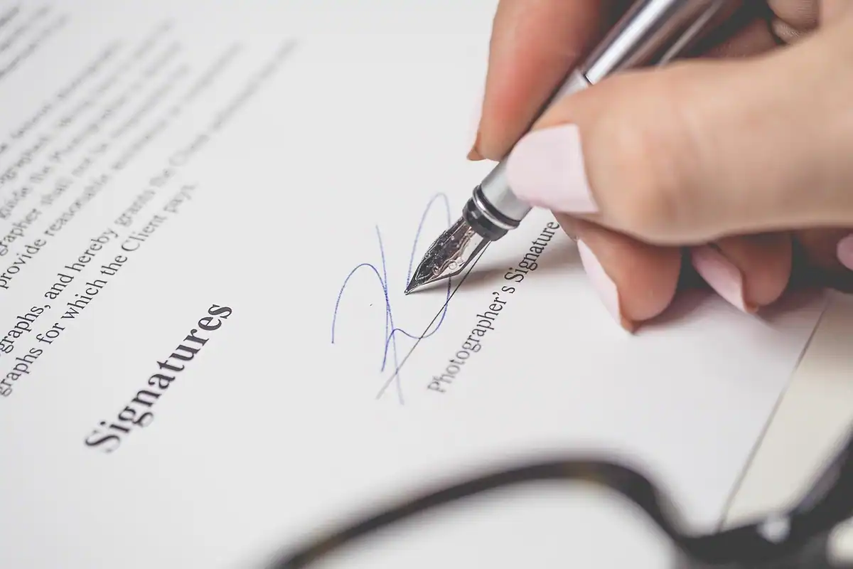Mână care semnează cu stiloul un document, în dreptul rubricii pentru semnătură