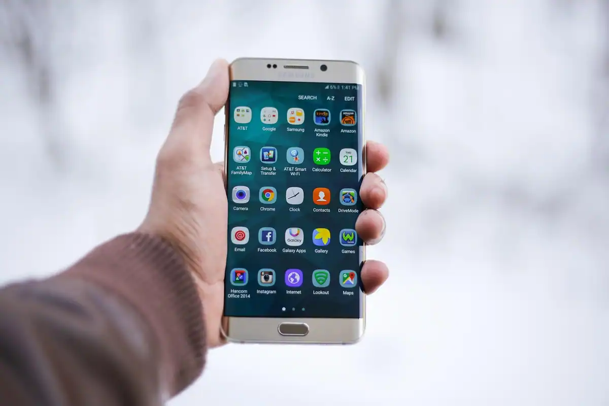 O mână ține un smartphone cu ecranul aprins, pe care se văd mai multe aplicații mobile