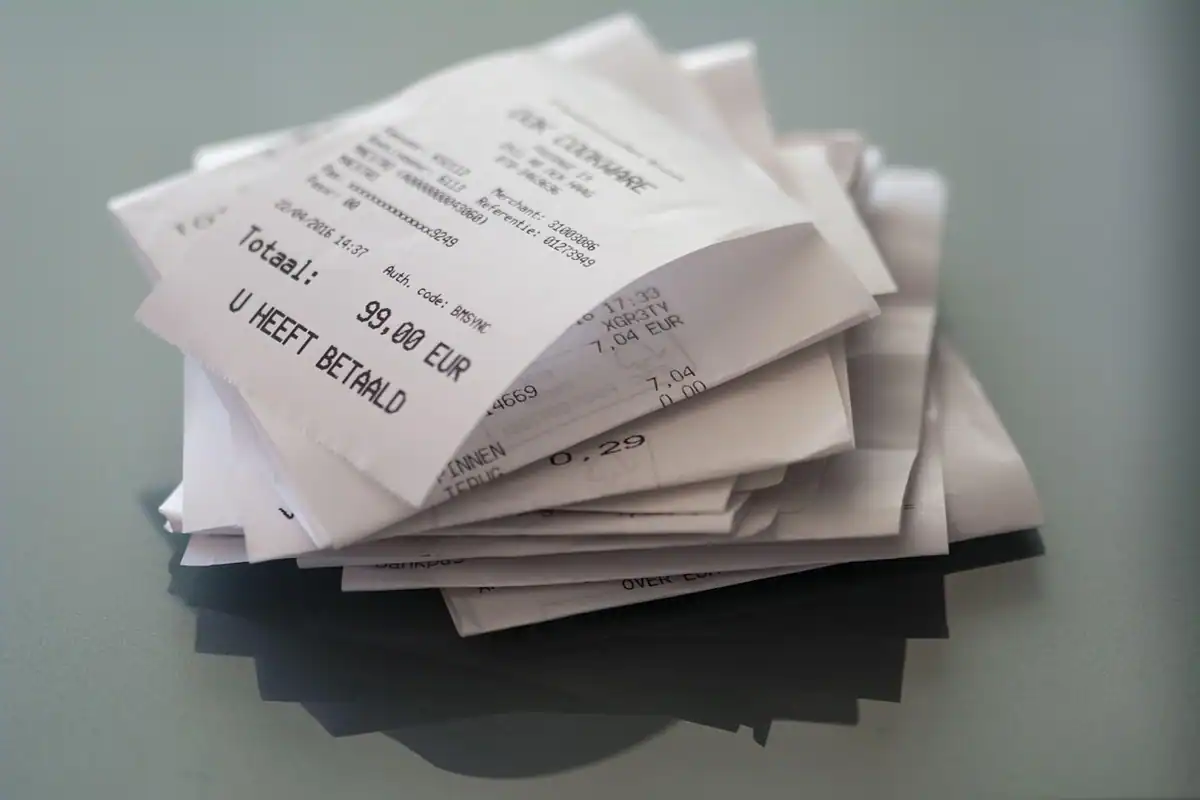 Un teanc de bonuri fiscale și bancnote de euro pe masă, simbol al cheltuielilor din gospodărie