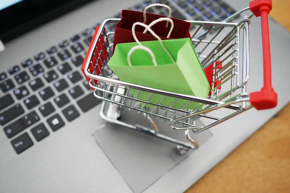 Coș de cumpărături cu pungi colorate așezat pe tastatura unui laptop, pentru cumpărături în rate
