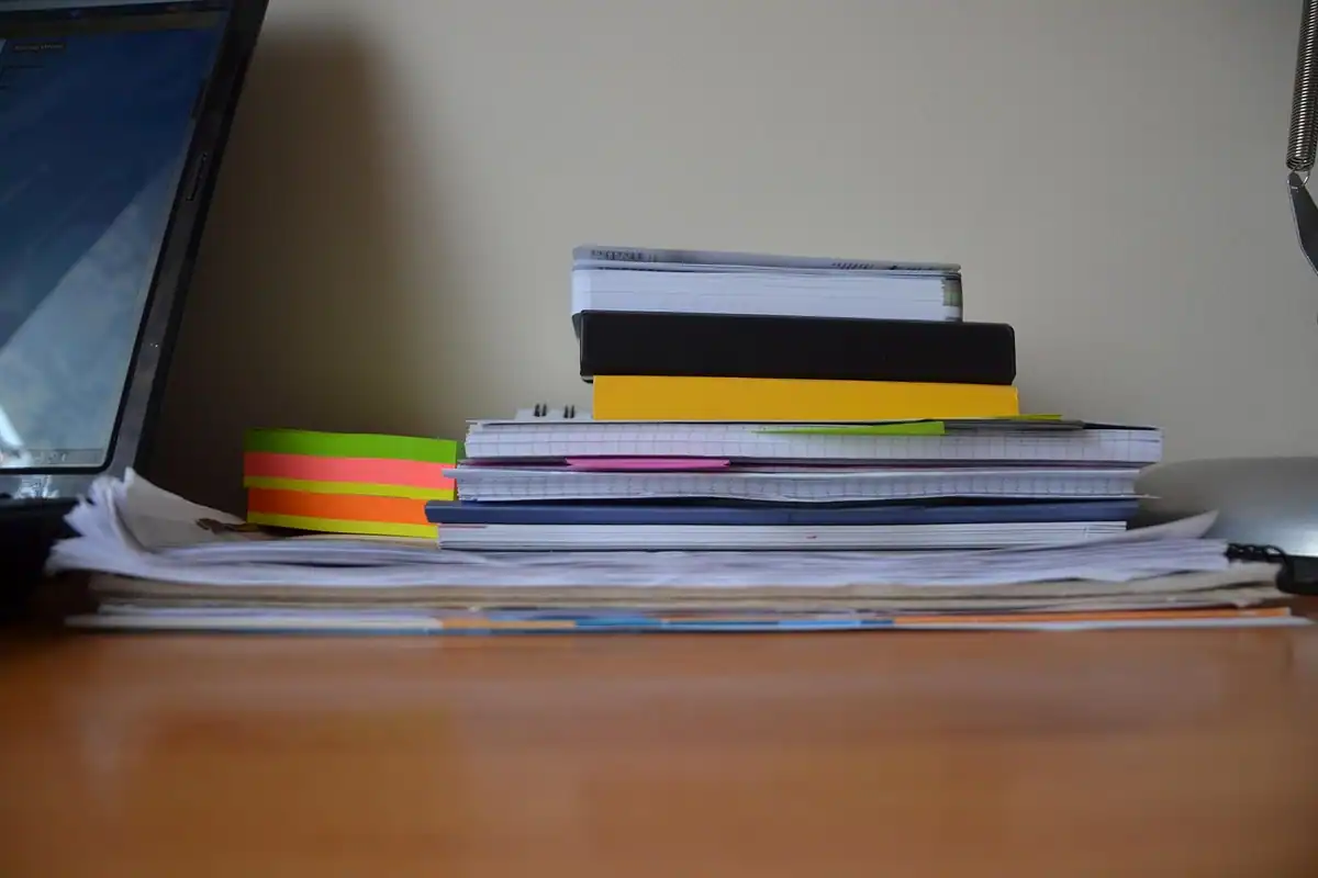 Teanc de cărți, caiete și hârtii pe un birou, lângă un laptop, pentru dosarul de credit