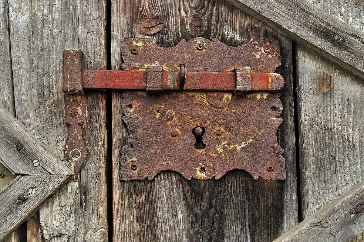 Poartă veche de lemn, ruginită și încuiată cu bare de fier, într-un decor rustic