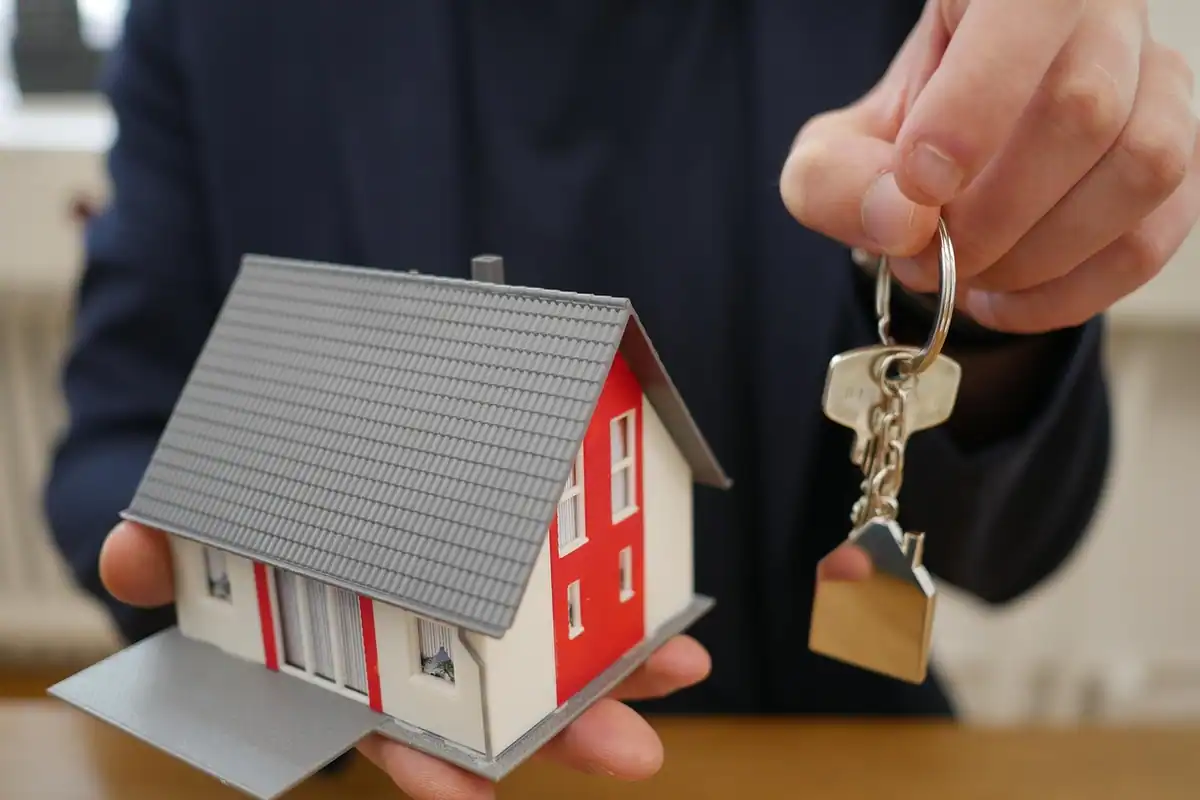 Model de casă cu acoperiș gri ținut în palmă, împreună cu cheile, pentru credit cu ipotecă