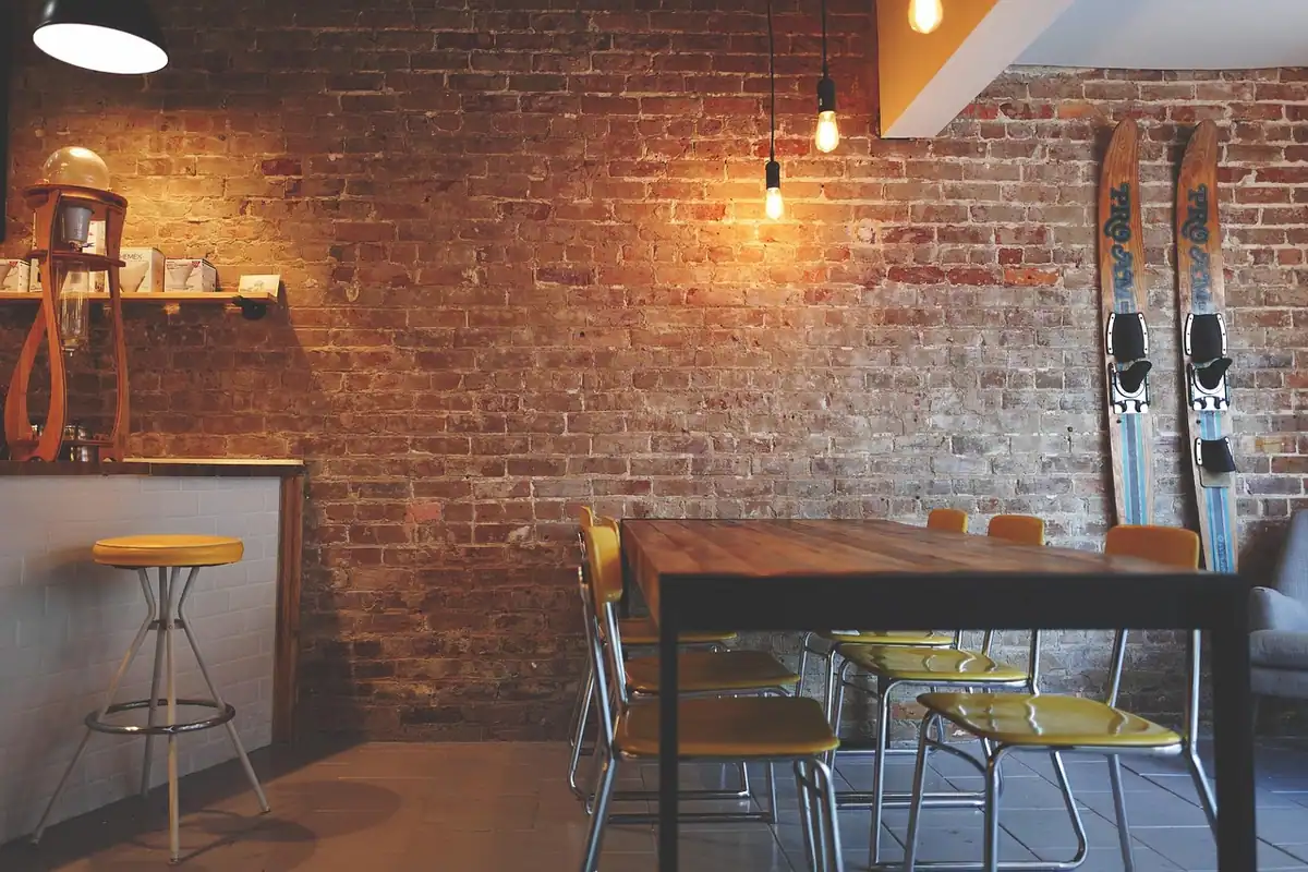 Interior de restaurant rustic, cu perete de cărămidă, mese, scaune și lumini calde