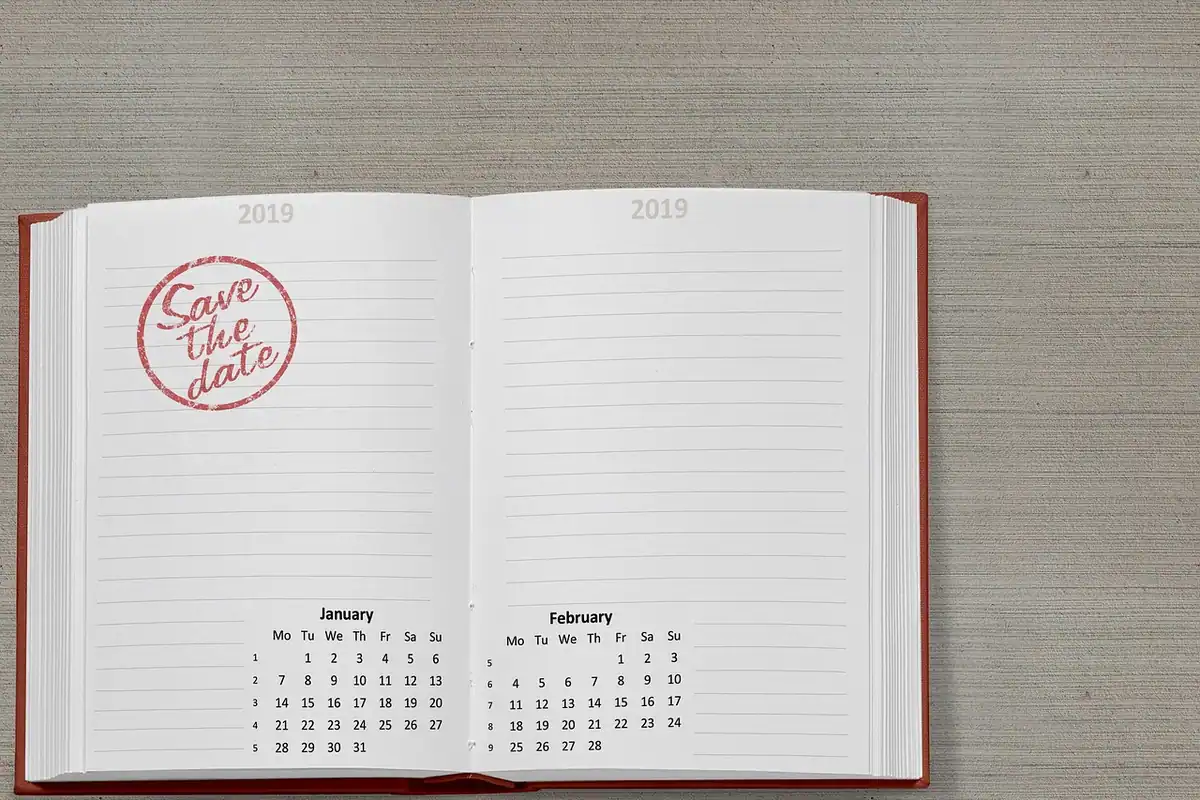 Un calendar deschis pe un birou, cu luni și zile, alături de un caiet pentru planificare
