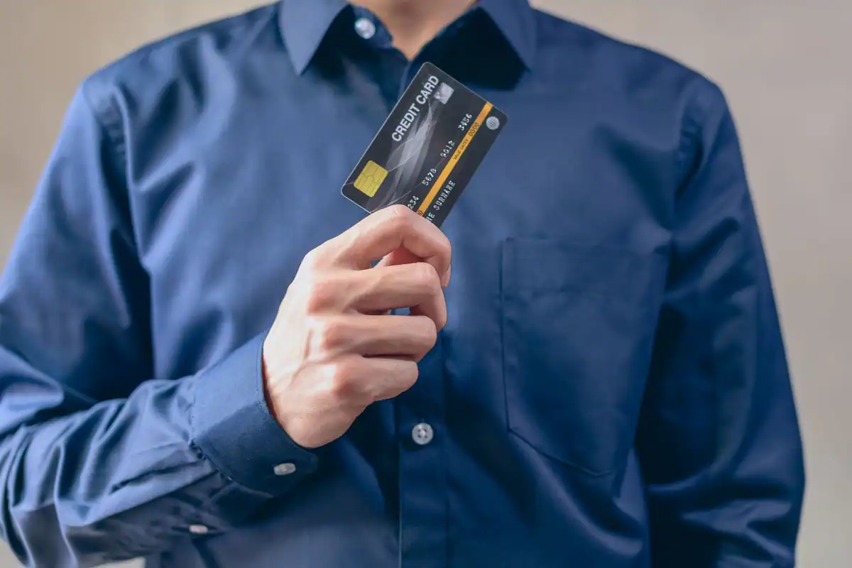 Bărbat în cămașă albastră care arată un card bancar negru, la primul credit