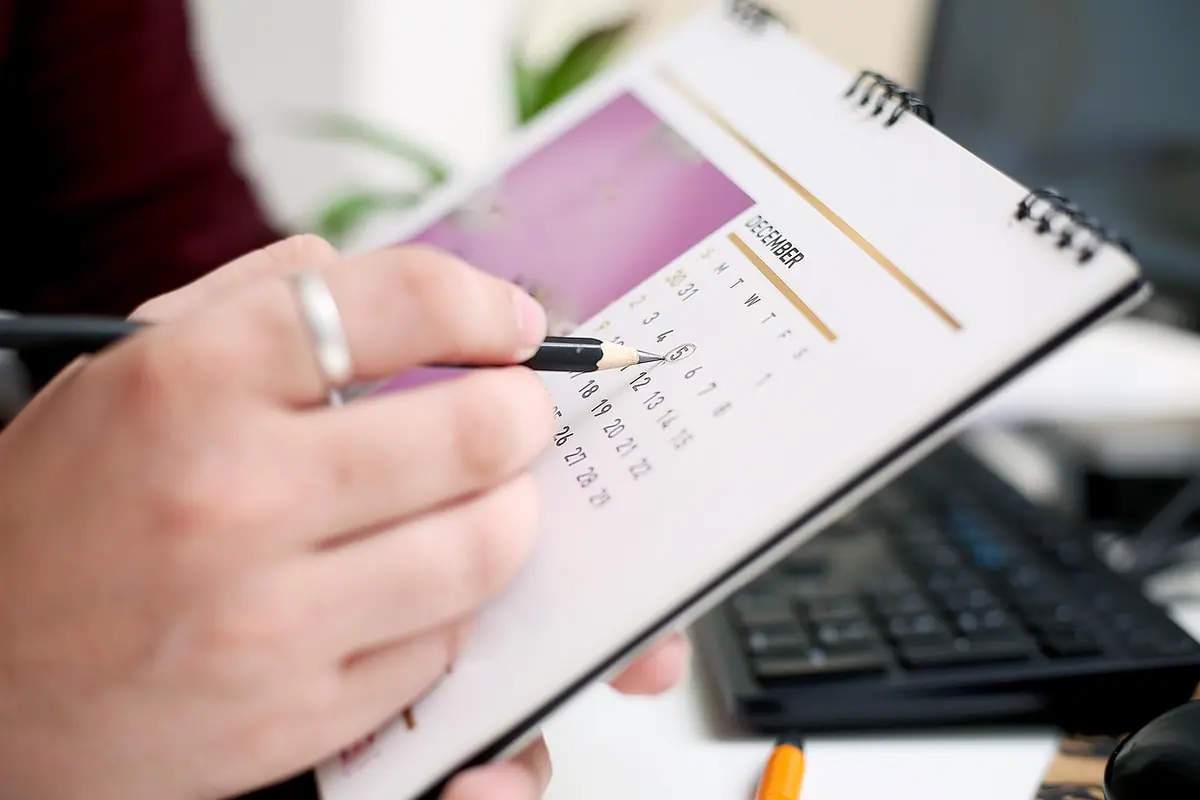 Mână cu pix deasupra unui calendar spiralat, pentru stabilirea datei ultimei rate