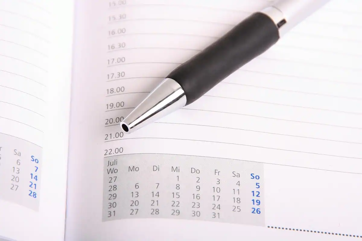 Un calendar, un pix și o foaie de hârtie pe un birou, folosite pentru planificarea întâlnirilor