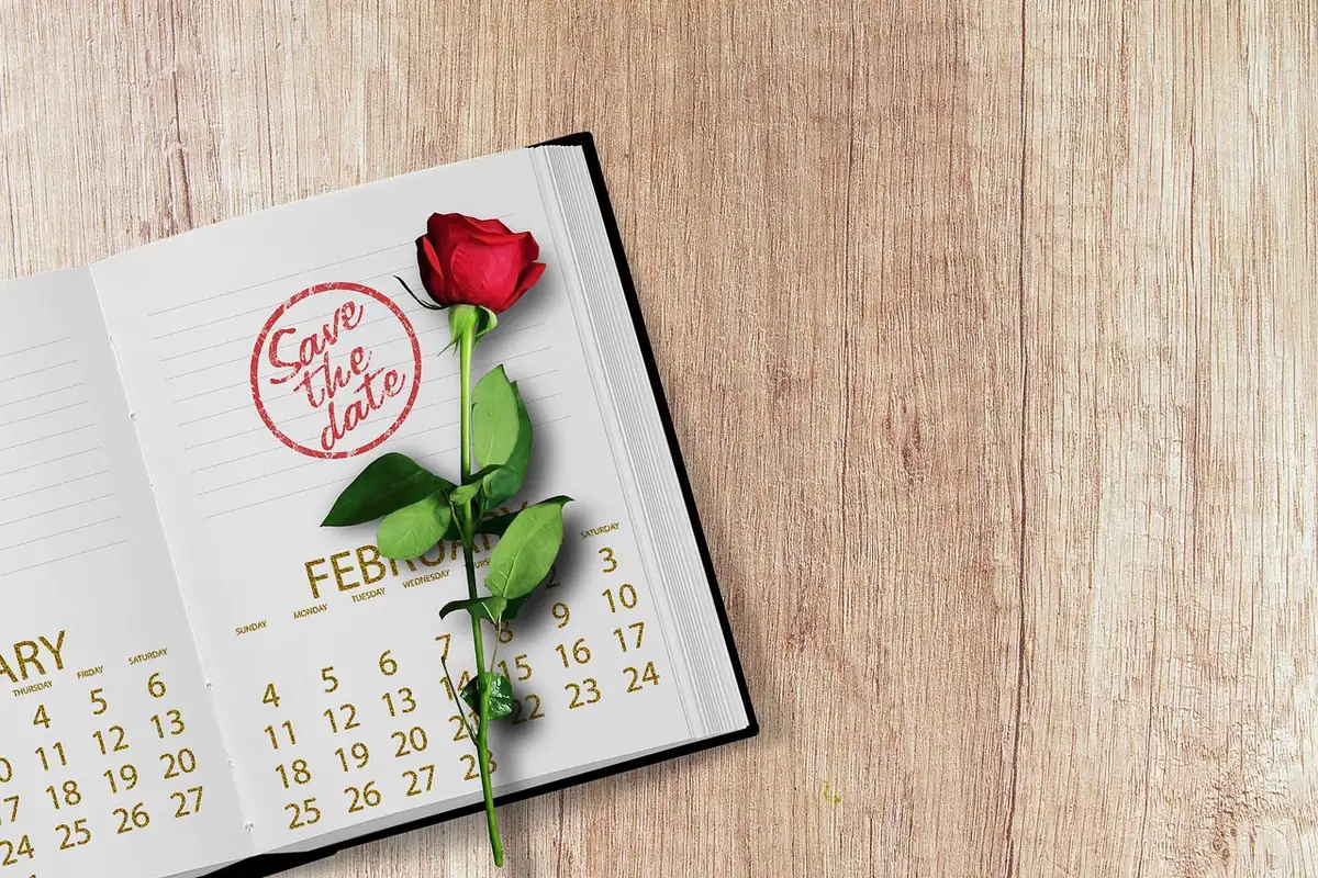 Calendar deschis pe o masă, cu zilele lunii, un trandafir și o ștampilă de cauciuc alături
