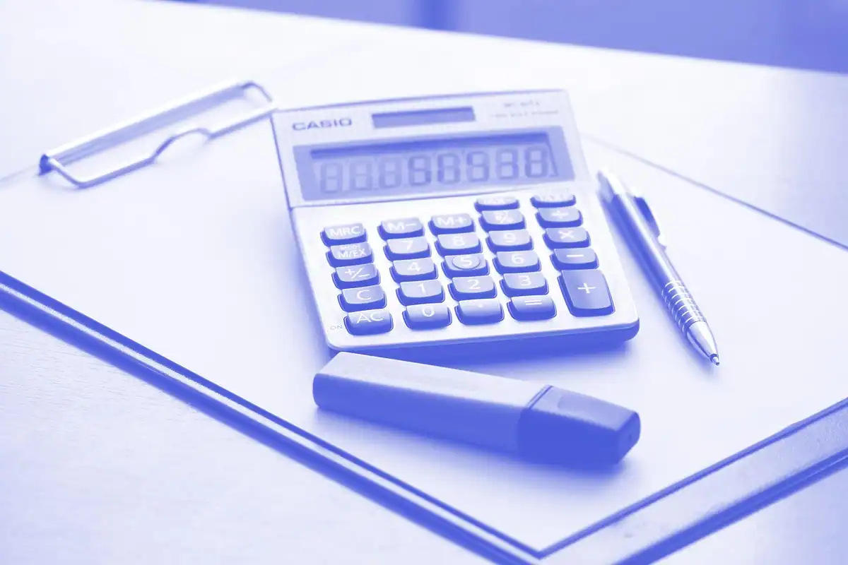 Calculator și stilou pe un clipboard cu tentă albastră, la calculul refinanțării