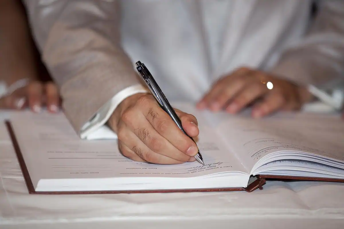 Mână cu stilou scrie într-un registru deschis, pentru semnarea actului adițional