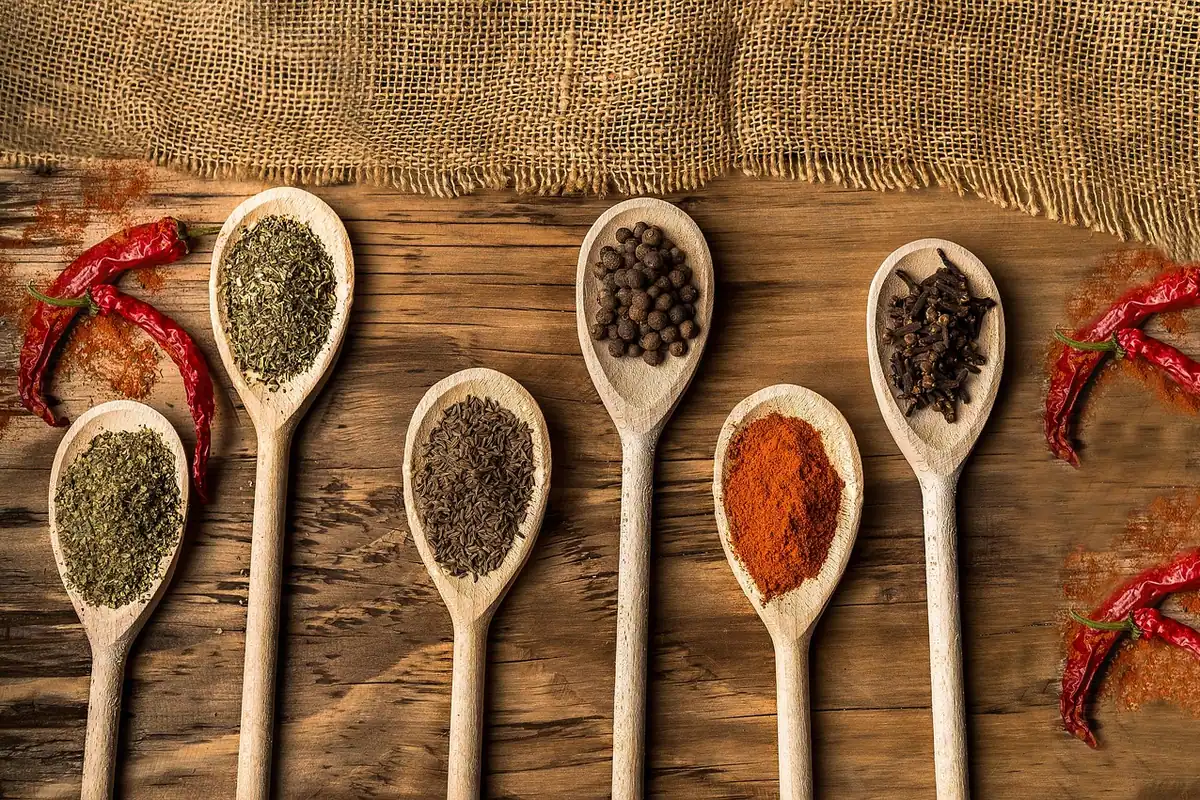 Mirodenii și ingrediente așezate pe o masă de bucătărie, lângă o lingură, cu piper