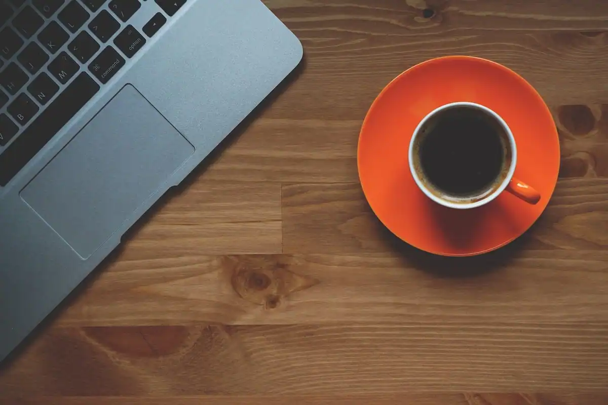 Cană de cafea lângă un laptop pe o masă de lemn, într-un spațiu de lucru de birou